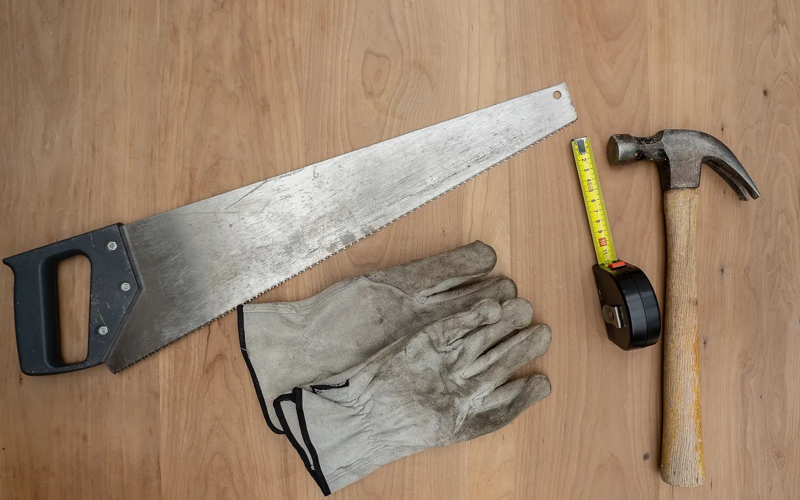 Sag, hammer, målebånd og arbeidshansker på en treflate